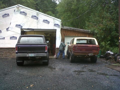 1979 Ford Bronco - Two Ford Broncos are parked outside a garage under construction.