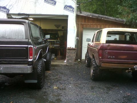 1979 Ford Bronco - Two Ford Broncos, a maroon 1979 model and a black one, are parked outside garages.