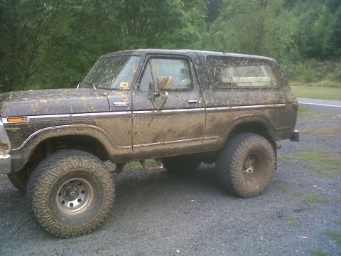 1979 Ford Bronco - This heavily soiled Ford Bronco is shown from the side, parked outdoors with trees in the background.