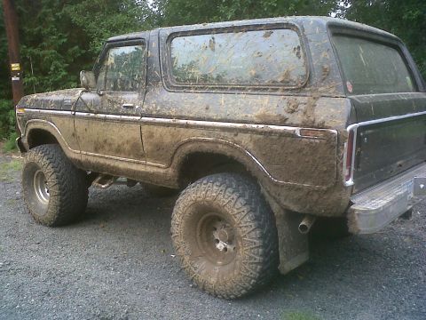 1979 Ford Bronco - This heavily mud-splattered SUV is viewed from the front-three-quarter angle, revealing its off-road modifications.