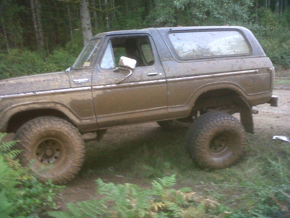 Brown lifted two-door Ford Bronco covered in mud in the woods