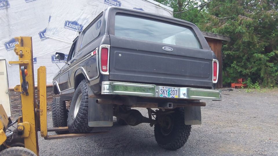 Rear view of a black 1978 Ford Bronco with an Oregon license plate SKY 207, being lifted by a yellow forklift