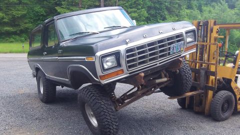 1979 Ford Bronco - A forklift is lifting the front end of a dark green Ford Bronco, showing its lifted suspension.