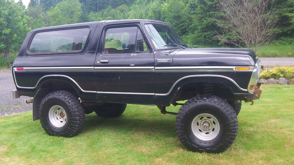 Black 1979 Ford Bronco lifted with off-road tires, parked on grass