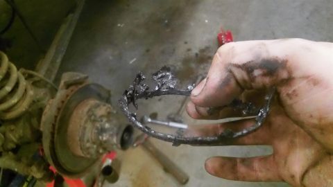 1979 Ford Bronco - A mechanic holds a damaged metal part, likely from a vehicle's drivetrain, with the suspension visible.