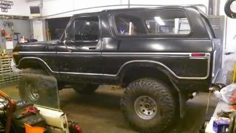 1979 Ford Bronco - This black Ford Bronco is parked inside a garage, showing its lifted suspension and off-road tires.