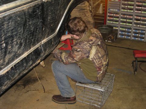 1979 Ford Bronco - A person works on the underside of a vehicle that is supported by a red jack in a garage.