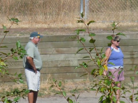 2006 Ford E350 - Two individuals stand in front of a wooden retaining wall with dry grass and foliage in the background.