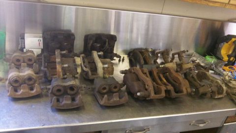 1979 Ford Bronco - Multiple brake calipers are laid out on a workbench, some appearing rusty and worn.