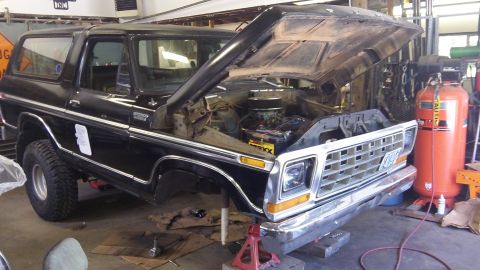 1979 Ford Bronco - A black 1979 Ford Bronco is shown with its hood up, revealing the engine bay, in a workshop setting.