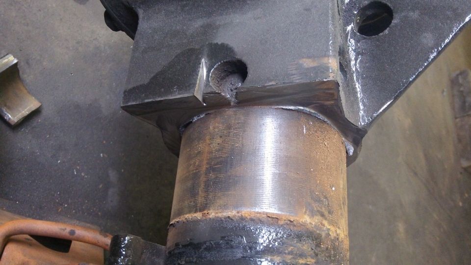 Close-up of a rusty metal cylinder attached to a black bracket with visible welds