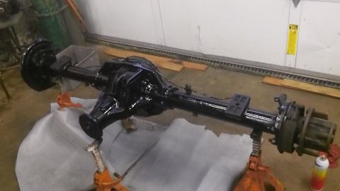 1979 Ford Bronco - A freshly painted rear axle assembly is supported by jack stands in a garage setting.