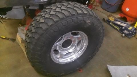 1979 Ford Bronco - A close-up view of a large off-road tire and chrome wheel, resting on wooden blocks in a garage.