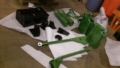 1979 Ford Bronco - Various green-painted automotive parts, including suspension components and jerry cans, are arranged on the floor.