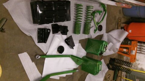 1979 Ford Bronco - Various green suspension components and fuel cans are arranged on a white covering on the floor.