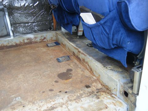 1988 Ford E350 - The interior of a van shows significant rust on the floor and worn blue seats.
