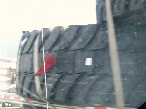 2006 Ford E350 - A large tire is strapped to a flatbed trailer, suggesting transport or storage.