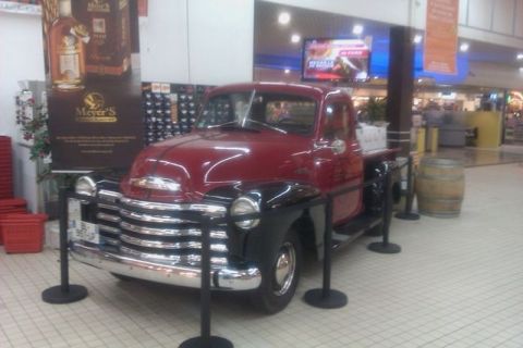 1991 Ford LTD Crown Victoria - A vintage red and black pickup truck is displayed inside a building with a barrel and promotional posters nearby.