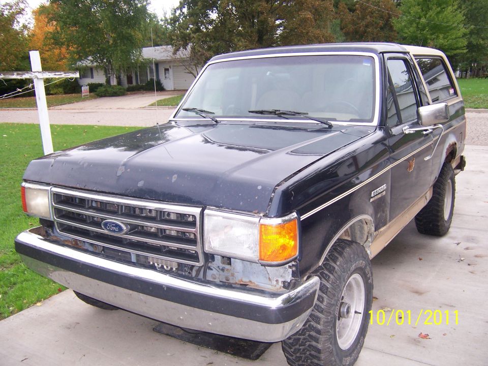 Dark blue Ford Bronco with a white top, parked in a driveway. The front end is visible