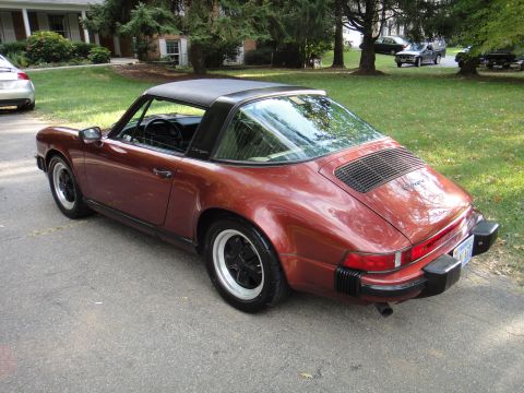 1986 Porsche 911 - A maroon Porsche 911 Targa is parked on a street, with other vehicles in the background.