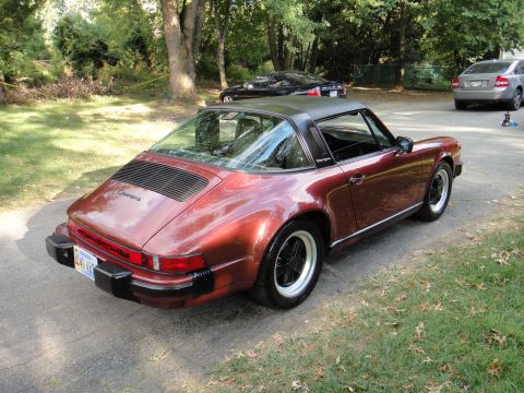 1986 Porsche 911 - This 1974 Porsche 911 Targa features a distinctive red metallic paint and a black targa top, seen here from a rear three-quarter perspectiv…