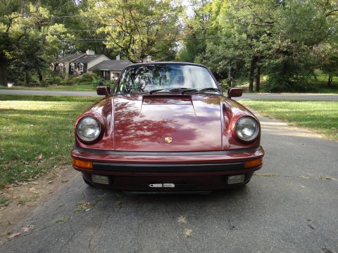 1986 Porsche 911 - A red 1986 Porsche 911 is shown from the front on a paved driveway with trees and houses in the background.