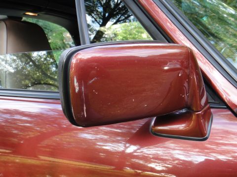 1986 Porsche 911 - Close-up of a red car's side mirror and door panel, with a watermark at the bottom right.