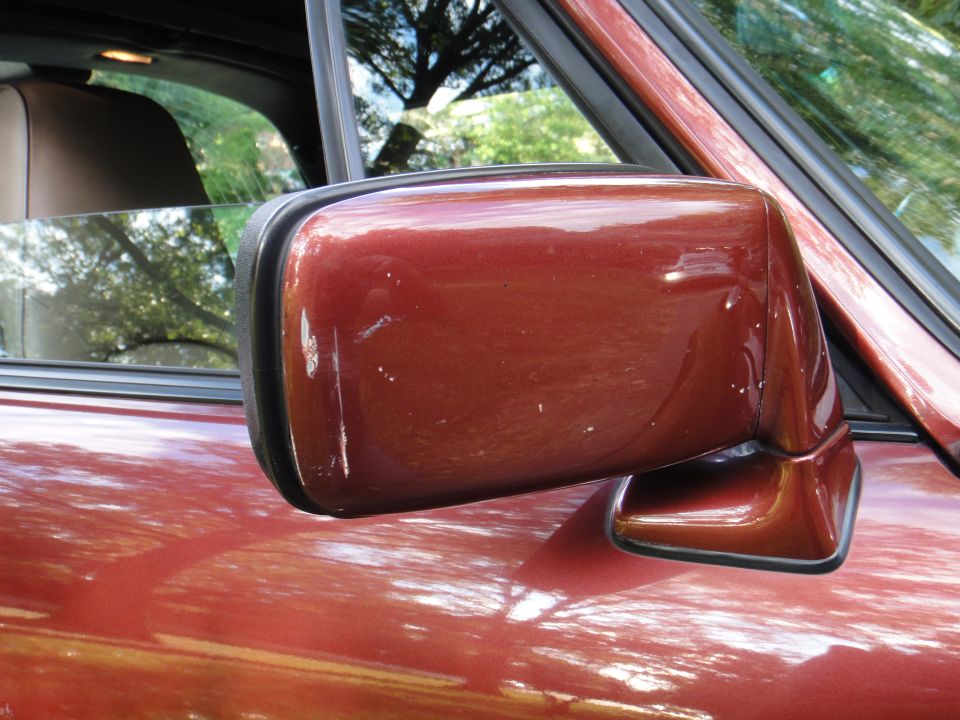 Red metallic car side mirror and door panel. Water spots visible on paint