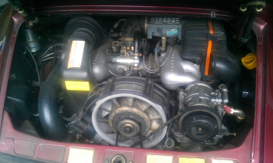 Rear engine bay of a burgundy air-cooled Porsche 911 flat-six with white cooling fan shroud