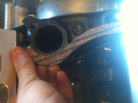 1993 Ford Bronco - A gasket is held in place against a dark engine part, with visible casting numbers and a SuperMotors watermark.