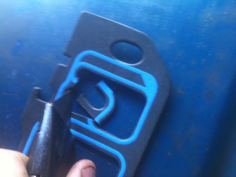 1993 Ford Bronco - A black gasket with blue sealant is being cut by a utility knife against a blue background.