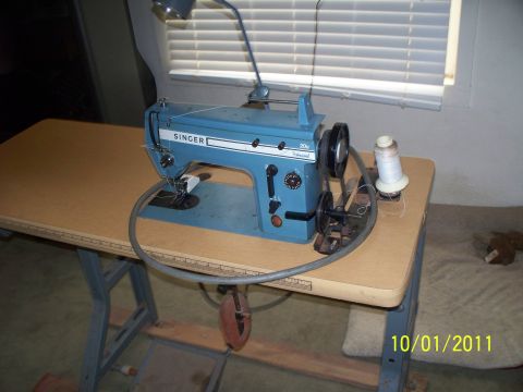 1990 Ford Bronco - A blue Singer sewing machine sits on a wooden table, with a spool of white thread nearby.
