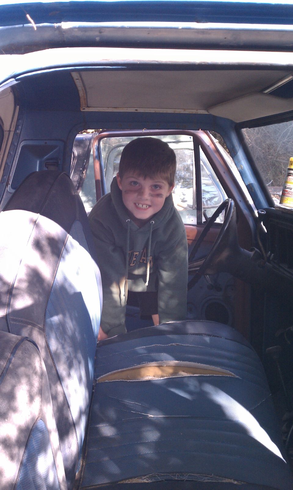 Interior view of a blue vehicle with a young boy, showing torn seats
