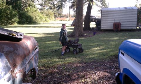 1979 Ford Bronco - A boy stands with a wagon next to heavily rusted vehicle parts in a yard.