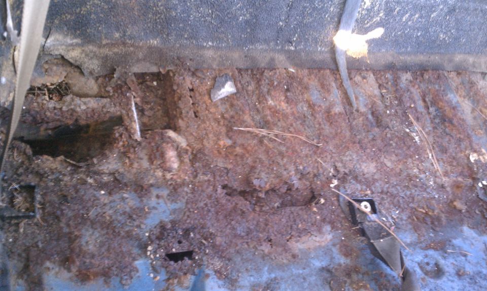 heavily rusted interior floor pan with holes and debris