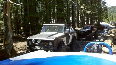 1971 Ford Bronco - Two off-road vehicles navigate a rocky, wooded trail.