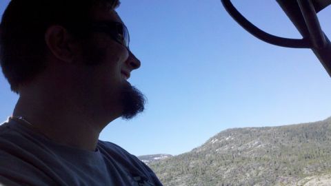 1971 Ford Bronco - A man with a goatee and sunglasses is seen from the side, with a mountain landscape under a clear blue sky.
