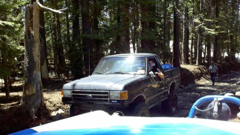 1971 Ford Bronco - A Ford pickup truck navigates a wooded trail, with another vehicle's interior visible in the foreground.