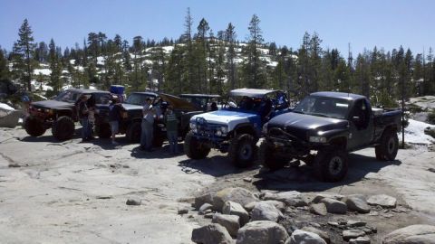1971 Ford Bronco - A group of heavily modified off-road vehicles are parked on a rocky, mountainous trail.