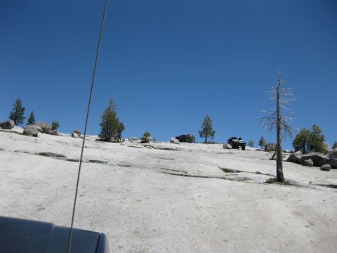1971 Ford Bronco - Off-road vehicles navigate a rocky, treed terrain under a bright blue sky.