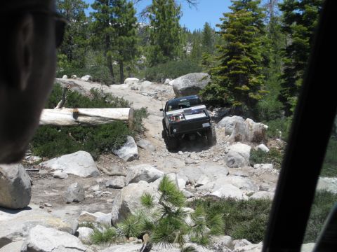 1971 Ford Bronco - A black truck is driving on a very rough, rocky path in a wooded area.