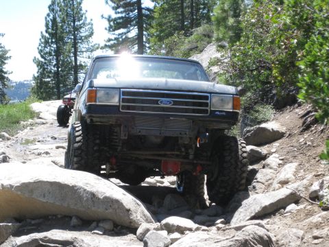 1971 Ford Bronco - A modified Ford truck tackles a challenging off-road path with another vehicle visible in the background.