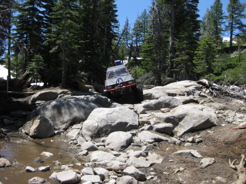1971 Ford Bronco - An off-road vehicle navigates a challenging rocky path in a wooded area.