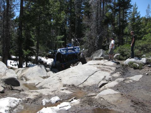 1971 Ford Bronco - A blue off-road buggy navigates a challenging rocky terrain in a forest setting.