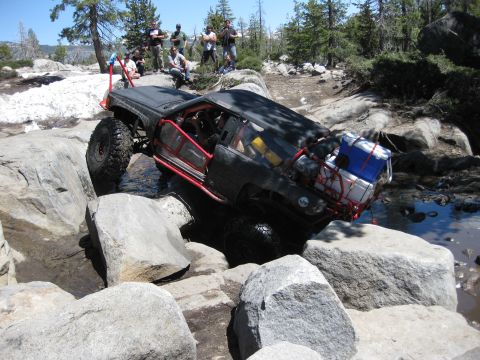 1971 Ford Bronco - An off-road vehicle with a red roll cage is shown traversing a challenging rocky and watery course.