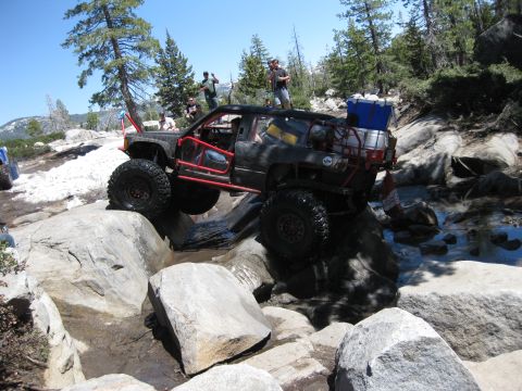 1971 Ford Bronco - This heavily modified SUV is tackling a challenging rocky terrain with water obstacles.
