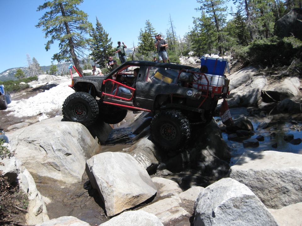 Modified off-road SUV navigating a rocky trail with people watching