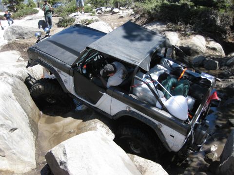 1971 Ford Bronco - An off-road vehicle attempts to traverse a rocky terrain with its cargo area filled with gear.