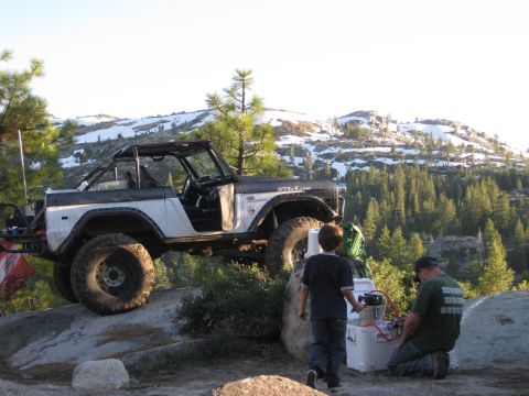 1971 Ford Bronco - A modified 1971 Ford Bronco is parked on a rocky incline with a mountainous backdrop.