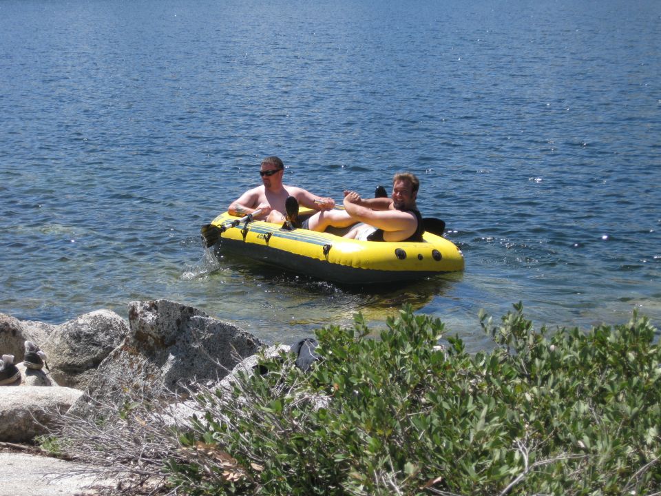 Two men relax in a yellow inflatable boat on a blue lake